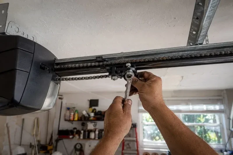 Hands holding a wrench against an opener trolley beneath a chain rail — Chain-Drive Opener Repair, London
