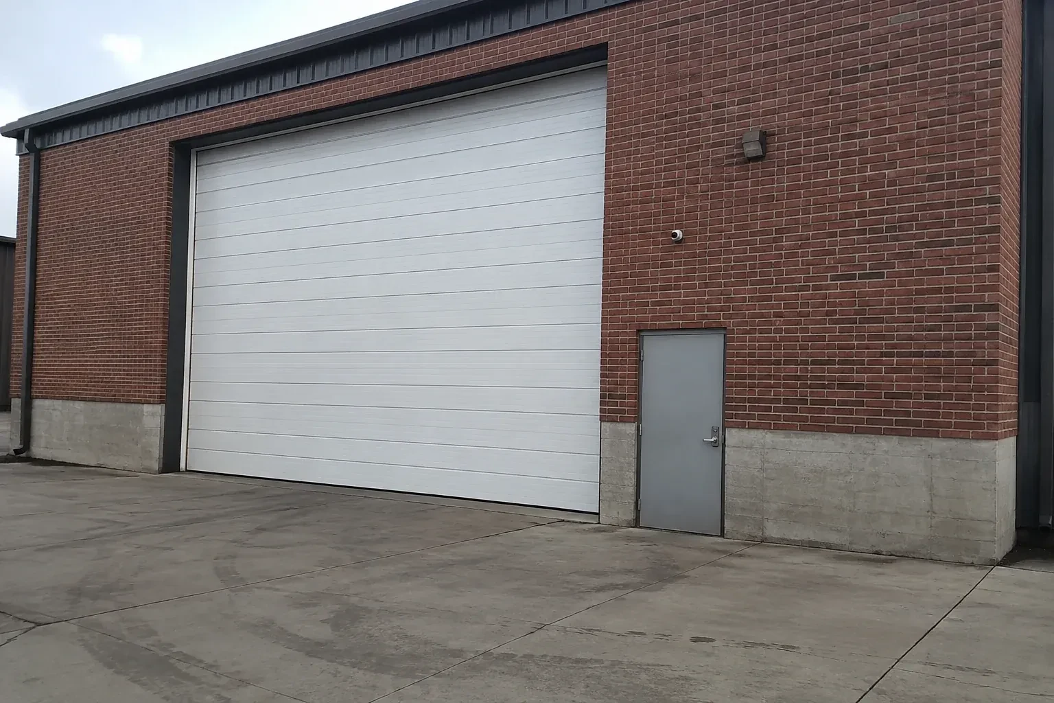 Tall closed sectional loading door beside a personnel door at a brick unit. — Commercial Sectional Door Repair, London