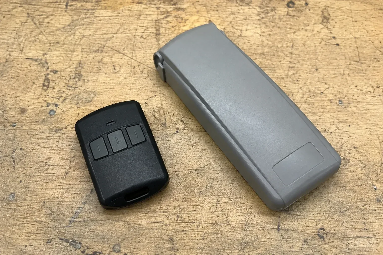 Three-button remote beside a closed grey keypad cover on a workbench. — Garage Door Remote and Keypad Programming, London