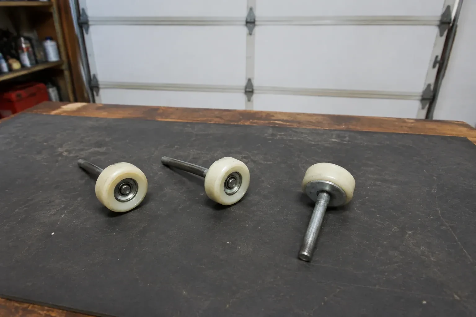 Three detached nylon-wheel garage door rollers with steel stems on a work mat. — Garage Door Roller Replacement, London
